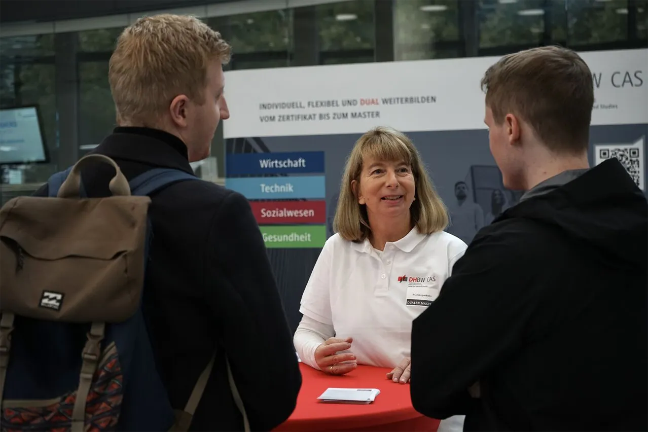 Eine Frau berät zwei Studierende an einem Stehtisch.